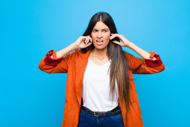 er boos, gestrest en geïrriteerd uitzien, beide oren bedekkend voor een oorverdovend geluid, geluid of luide muziek