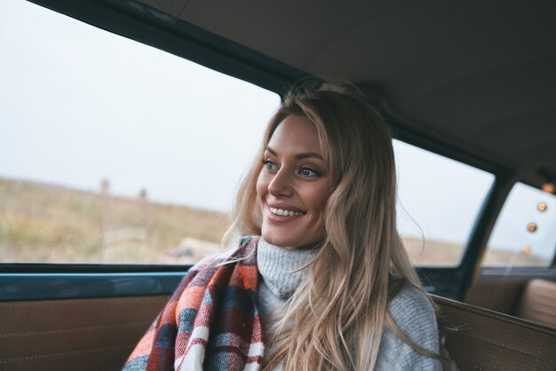 Er even tussenuit... Aantrekkelijke jonge vrouw die uit het raam van de bus kijkt en glimlacht terwijl ze op de passagiersstoel voorin zit