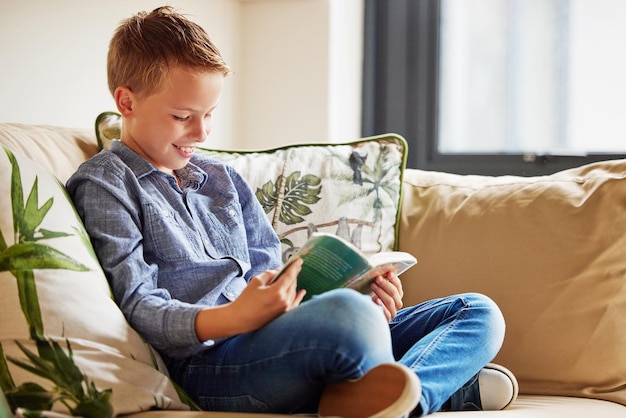 Er gaat niets boven het ontdekken van de levens die in pagina's leven. Shot van een schattig jongetje dat alleen thuis op de bank zit en een boek leest