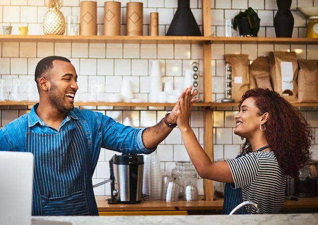 Foto er is niets dat ze niet samen kunnen doen bijgesneden opname van een aanhankelijk jong stel dat high five geeft terwijl ze in hun koffieshop staan