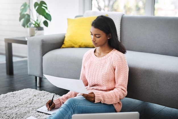 Er is niets mis met in het weekend werken Bijgesneden opname van een jonge, mooie vrouw die door papierwerk gaat en een laptop gebruikt terwijl ze thuis op de grond in de woonkamer zit