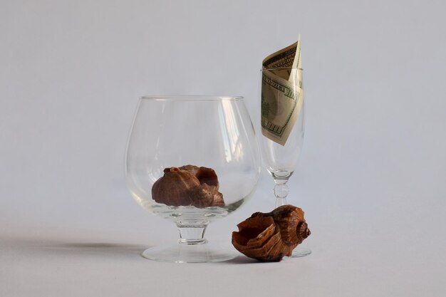 Er staan twee glazen op tafel in het ene glas een schelp in een ander glas een dollarbiljet