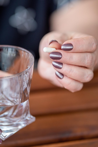 er staat een glas water op tafel, oudere vrouw met een medicijncapsule in haar hand