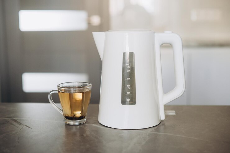 Er staat een witte plastic theepot op de tafel samen met een beker voor het brouwen van thee