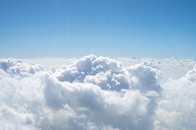 Er zijn veel witte wolken tussen de blauwe lucht. Deze weergave komt vanuit het raam van het vliegtuig.