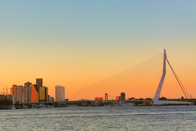 Erasmus brug over de rivier de Maas met wolkenkrabbers in Rotterdam, Zuid-Holland, Nederland tijdens schemeringzonsondergang.