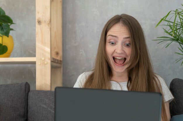 Erg blij en verrast vrouw met laptop. Vrouw verheugt zich zittend op de laptop. Onverwachte overwinning.