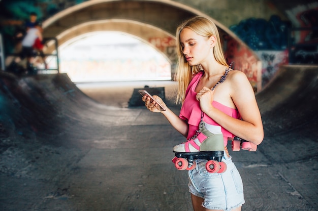 Ernstig en geconcentreerd meisje staat en houdt de telefoon in de hand. Ook houdt ze rollen vast die over de schouder hangen. Ze kijkt naar de telefoon. Ze wacht op een telefoontje