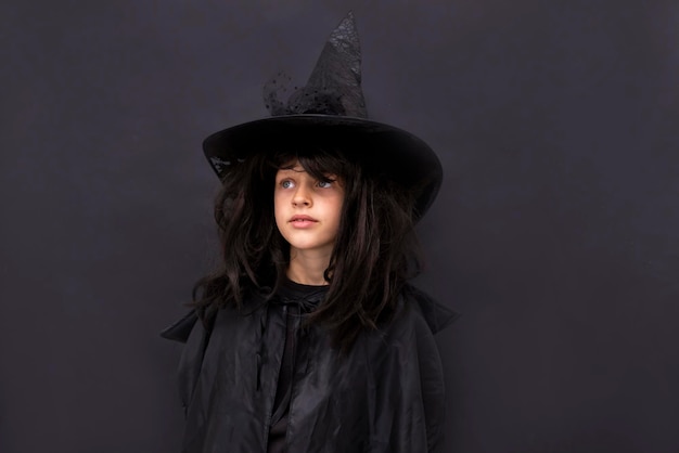 Ernstig Halloween-kind op zwarte achtergrond Kind in zwart tovenaarskostuum met lang haar mysterieuze heksentruc of vrolijk behandelen Jongen in een kostuumwizard Kopieer ruimte
