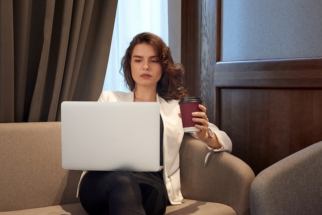 Ernstig jong meisje die aan laptop werken en koffie drinken