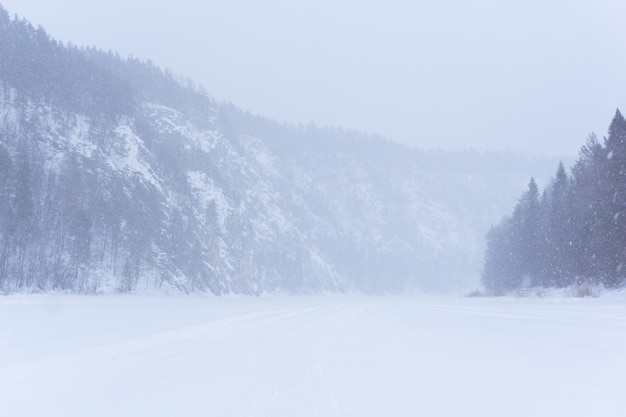 Ernstig noordelijk landschap - een rotsachtige vallei van een bevroren winterrivier tijdens een sneeuwstorm