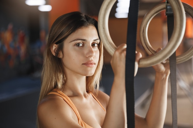 Ernstig ogende gemotiveerde en vastberaden close-up geschoten vrouw die gerichte camera kijkt, crossfit-ringen vasthoudt.