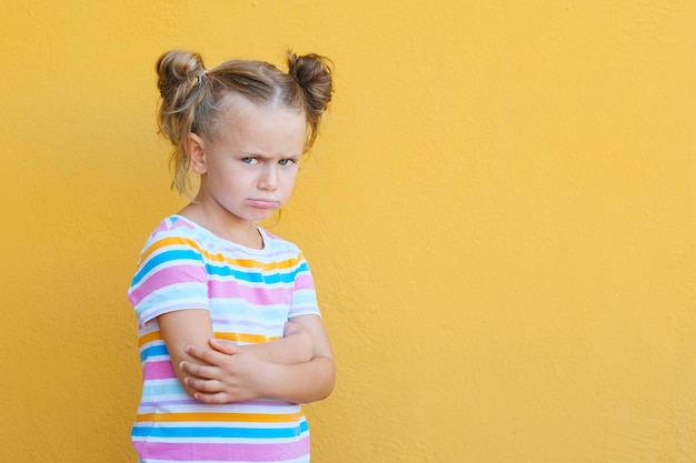 Ernstig peinzend klein meisje dat ongelukkig naar de camera kijkt, van streek is voorschoolse kind melancholisch of verveeld geïsoleerd over gele studio-achtergrond