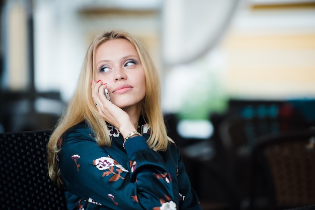 Ernstige aantrekkelijke jonge vrouw praten op mobiele telefoon in café