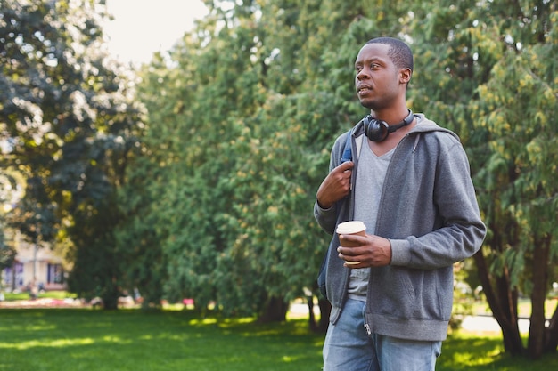 Ernstige afro-amerikaanse student met afhaalkoffie in het park buiten, met rust op de campus. Onderwijsconcept, kopieer ruimte