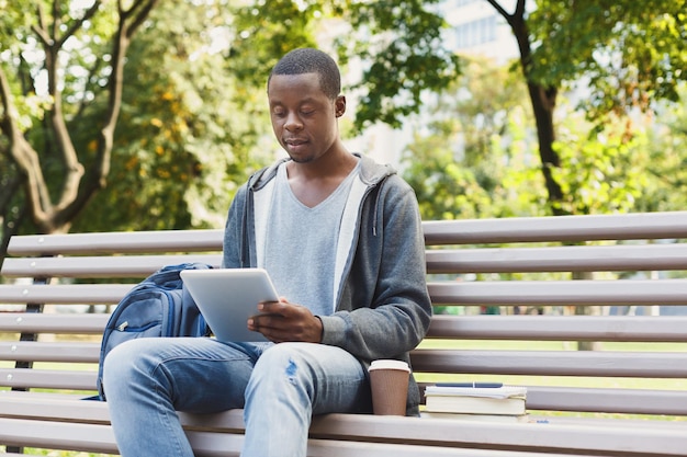 Ernstige Afro-Amerikaanse student met tablet buitenshuis. Casual student die e-mail controleert en op internet surft op een digitaal apparaat in het park. Technologie, sociale media, onderwijs en freelance concept.