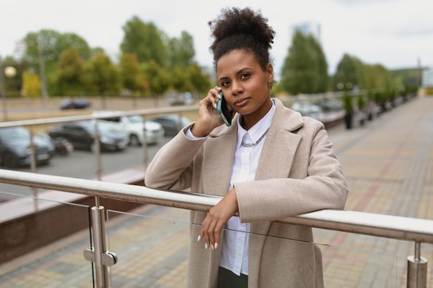 Ernstige Afro-Amerikaanse vrouw advocaat in een beige jas op de achtergrond van de stad spreekt op a