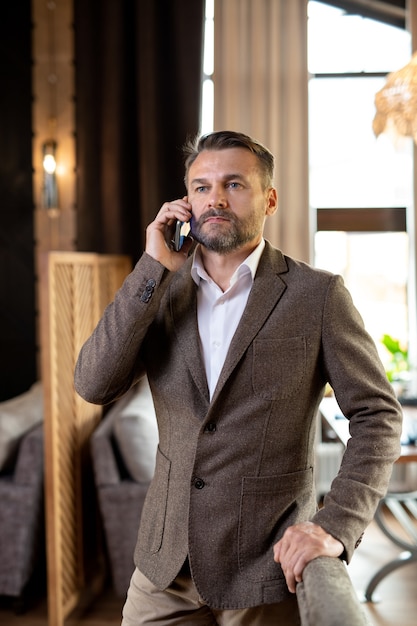 Ernstige agent die met mobiele telefoon naar zijn cliënt luistert terwijl hij aan tafel in een luxe restaurant staat