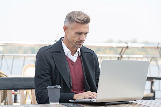 Ernstige baas die online werkt in een laptop die koffie drinkt op het terras