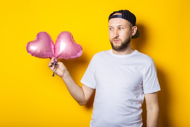 Ernstige bebaarde jonge man met roze hart lucht ballonnen