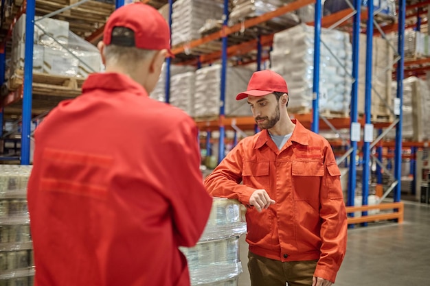 Ernstige bebaarde jongeman leunend op de pallet met vracht voor zijn collega