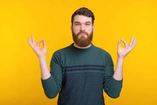 Ernstige bebaarde man probeert yoga te beoefenen en zenon gele ruimte te bereiken.