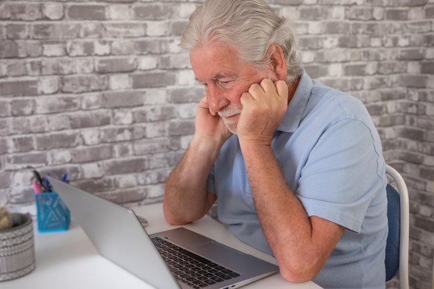 Ernstige bezorgde zakenman die naar laptop kijkt met de handen op het gezicht van een oudere man die op de werkplek zit