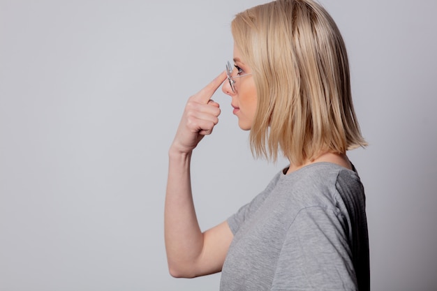 Ernstige blonde vrouw in glazen op witte muur