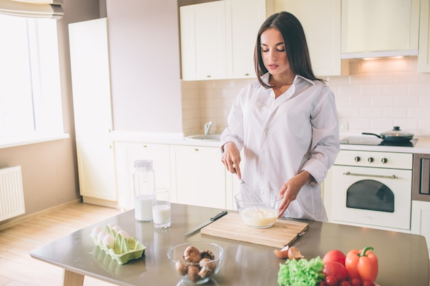 Ernstige en geconcentreerde jonge vrouw staat in de keuken en koken.