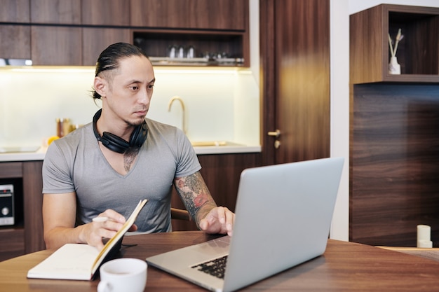 Ernstige fitte man die informatie op het laptopscherm controleert en aantekeningen maakt in de planner wanneer hij thuis werkt vanwege een pandemie van het coronavirus