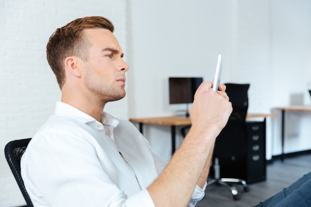 Ernstige geconcentreerde jonge zakenman die tablet op het werk zit en gebruikt