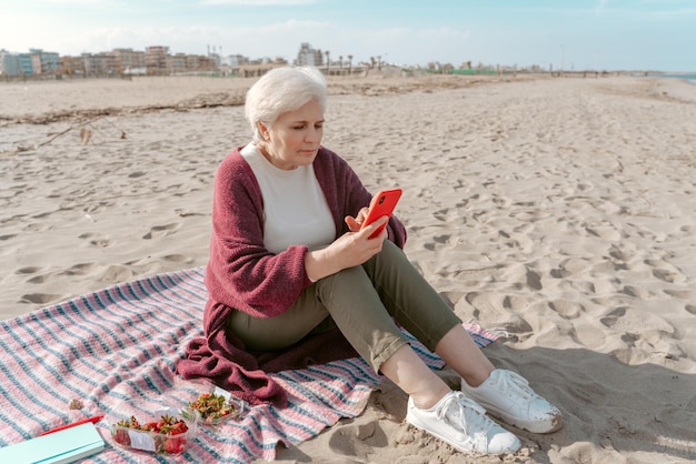Ernstige gefocuste dame die op het zand zit en naar de smartphone in haar handen kijkt