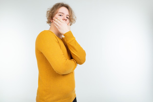 Ernstige golvende blonde jonge man staat nadenkend op een wit