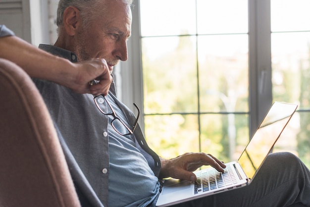 Ernstige hogere mens die laptop thuis met behulp van