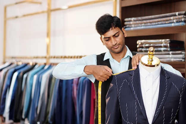 Ernstige Indiase kleermaker die metingen doet van op maat gemaakte colbert op mannequin