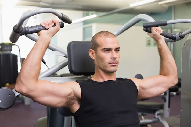 Ernstige jonge man aan het werk op fitness machine op gymnasium