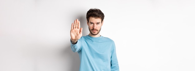 Ernstige jonge man die er zelfverzekerd uitziet met uitgestrekte hand en zegt: stop, verbied iets ergs of gi