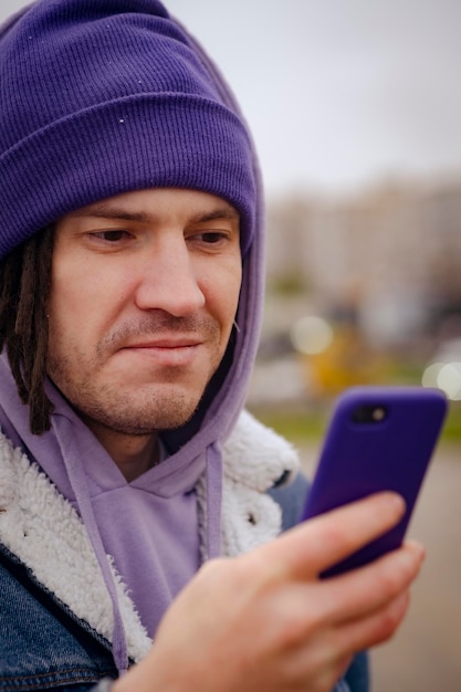 Ernstige jonge man in warme kleren die op mobiele telefoon surft terwijl hij in de winter op straat in de stad staat