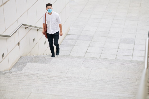 Ernstige jonge man met medisch masker loopt de trap op in de stad