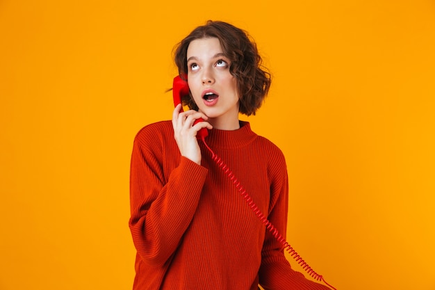 ernstige jonge mooie vrouw poseren geïsoleerd op gele muur praten via de telefoon.