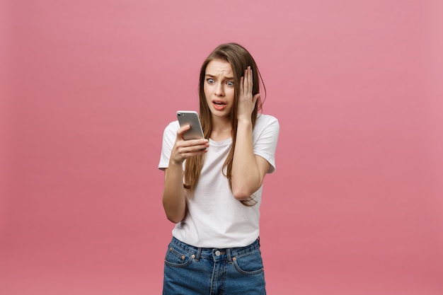 Ernstige jonge vrouw die op telefoon spreekt die op roze wordt geïsoleerd.