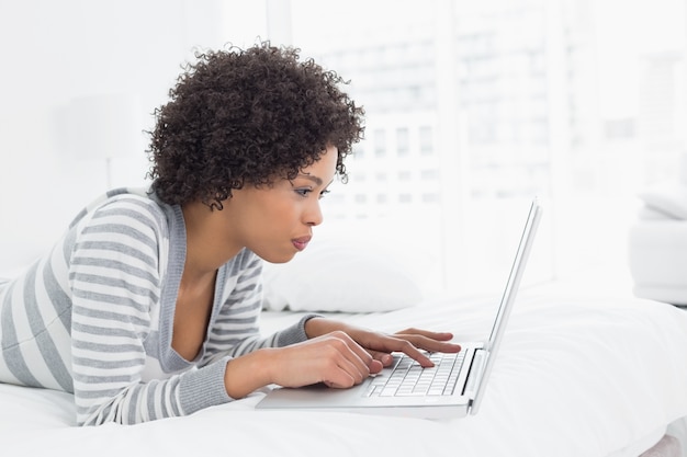 Ernstige jonge vrouw met laptop in bed