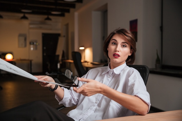 Ernstige jonge vrouw modeontwerper met een bril en kijken naar schetsen op kantoor