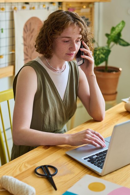 Ernstige jongedame met smartphone op het gehoor in gesprek met cliënt voor laptop