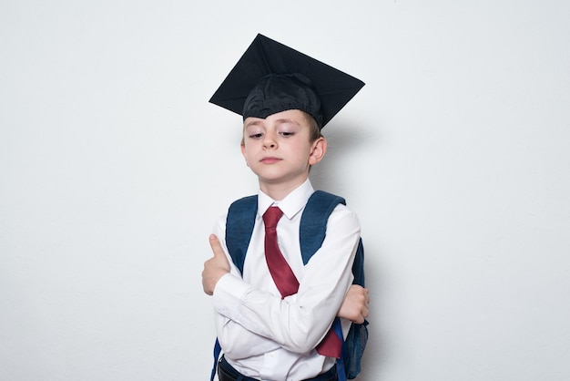 Ernstige jongen in schooluniform en afgestudeerde hoed op witte achtergrond Junior High School education