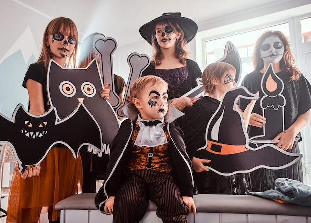 Ernstige kinderen in Halloween-kostuums poseren voor de fotograaf terwijl ze versieringen vasthouden.