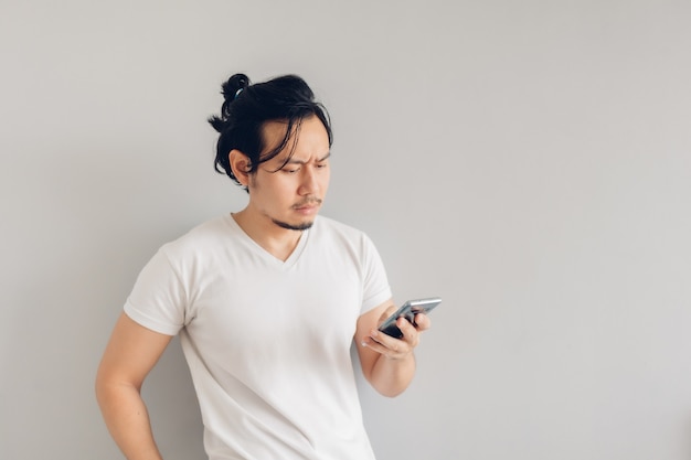 Ernstige lange haren man in wit casual t-shirt gebruikt smartphone.