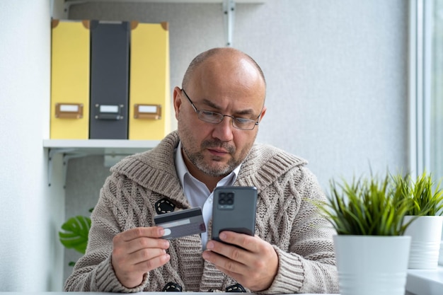 Ernstige man met een bril die online met creditcard betaalt via de telefoon