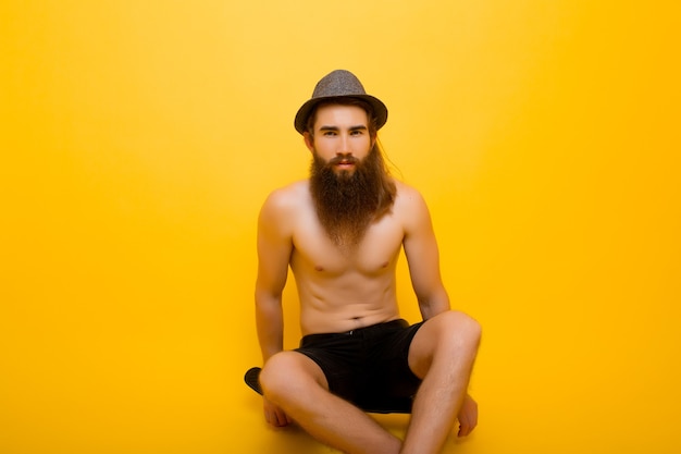Ernstige man met lange baard zit op een stuiverbord op gele muur.