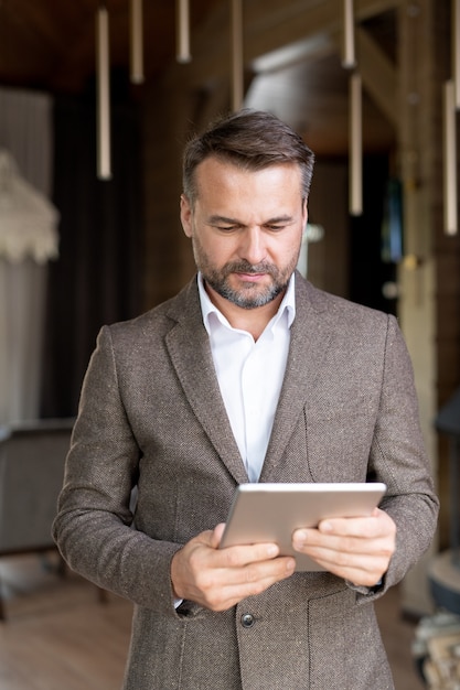 Ernstige mannelijke ondernemer die in formalwear touchpad voor zich houdt en in het net voor informatie surft